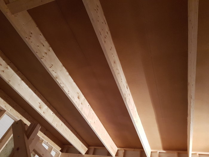 Takstolar och masonitplattor monterade i ett tak under konstruktion i en byggmiljö.