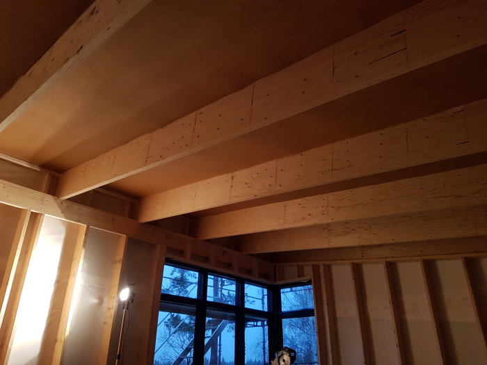 Nyinstallerad masonit i taket av ett halvfärdigt byggprojekt, med synliga träreglar och ett fönster.