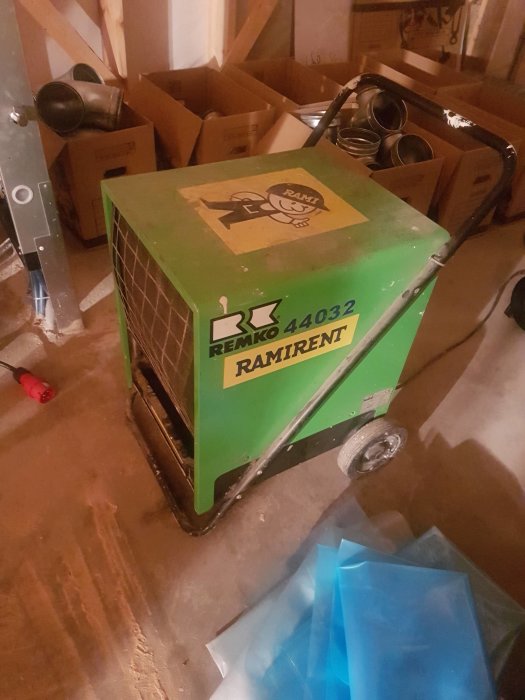Avfuktare av märket REMKO på ett bygge med kartonger och byggmaterial i bakgrunden.