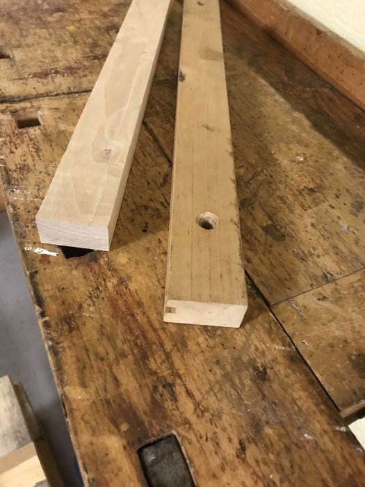 Björkträbitar på en arbetsbänk, en ej bearbetad och en med urfräst spår.