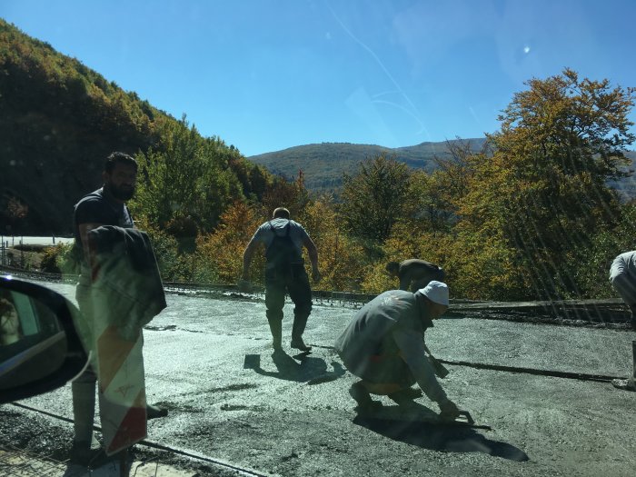 Arbetsmän som jämnar ut betong vid vägbygge med berg och höstträd i bakgrunden