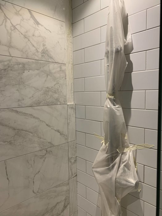 Ett hörn av ett halvfärdigt badrum med kombination av marmorliknande och vita kakelplattor, skyddad sanitetsinstallation.