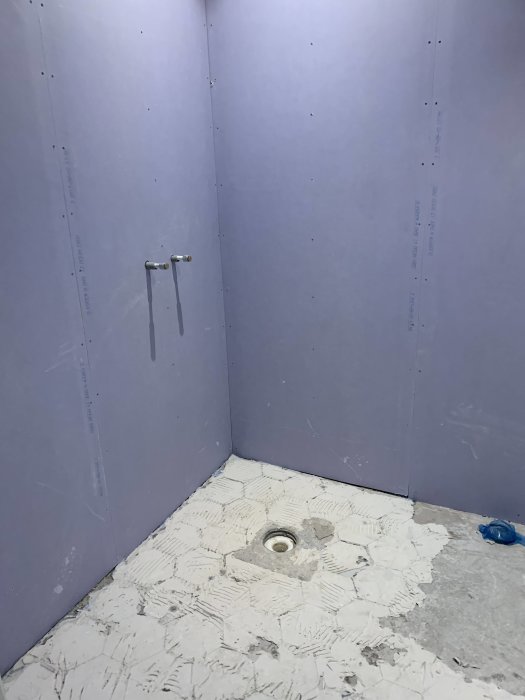 Ett underkonstruerat badrum med violett väggskivor och ett ofullständigt kaklat golv med golvbrunn.