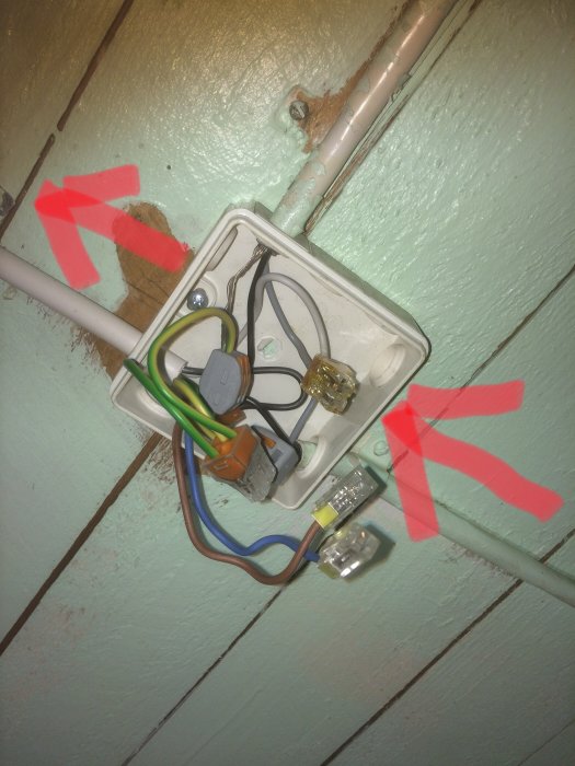 Öppen eldosa med olika färgade kablar och en Wago-koppling, markerat med röda pilar som visar strömriktningen.