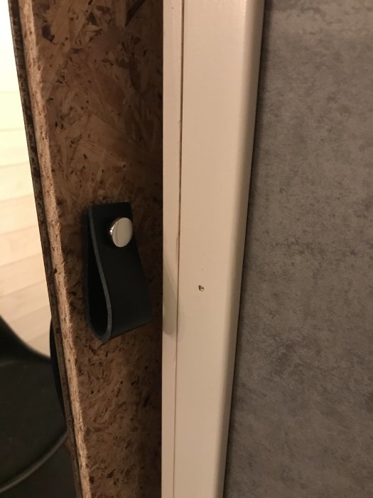 Rostig skjutdörr med rå OSB-baksida och svart läderflärp som handtag, detaljvy.