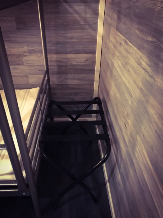 Laminatklädda väggar med svart väskhållare och ljusinsläpp i en kompakt, modern sovrumsmiljö.
