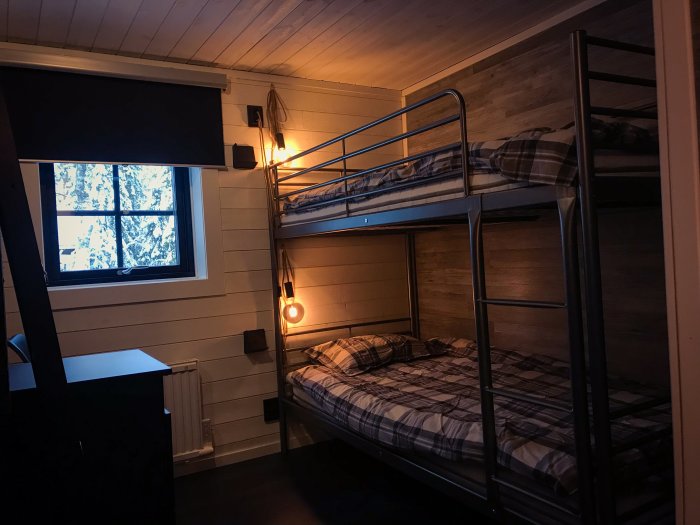 Praktiskt sovrum med våningssäng, träinredning och synlig radiator under ett fönster med vinterutsikt.