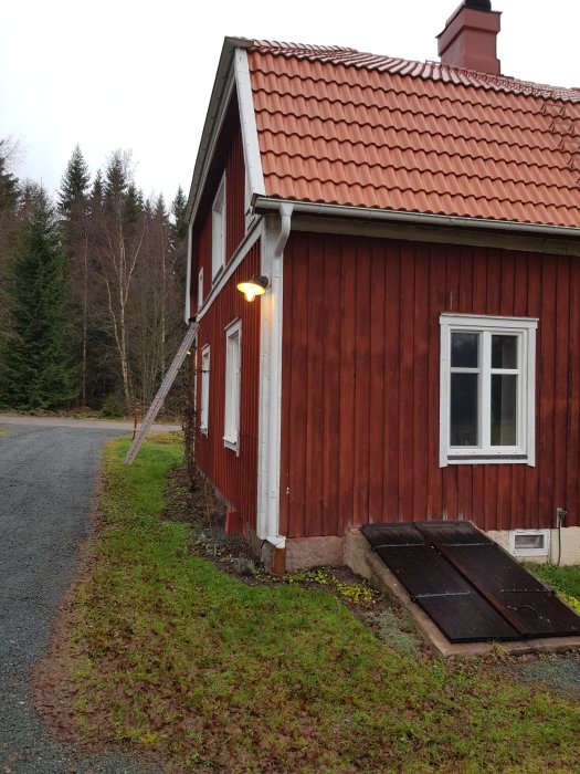 Utelampa tänd på rödfärgat hus med tegeltak som gör hörnet ljusare.