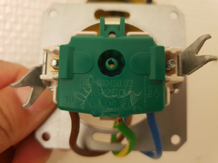 Närbild på en eluttagets baksida med synliga anslutningar och en grön plastdel, saknande frontplatta.