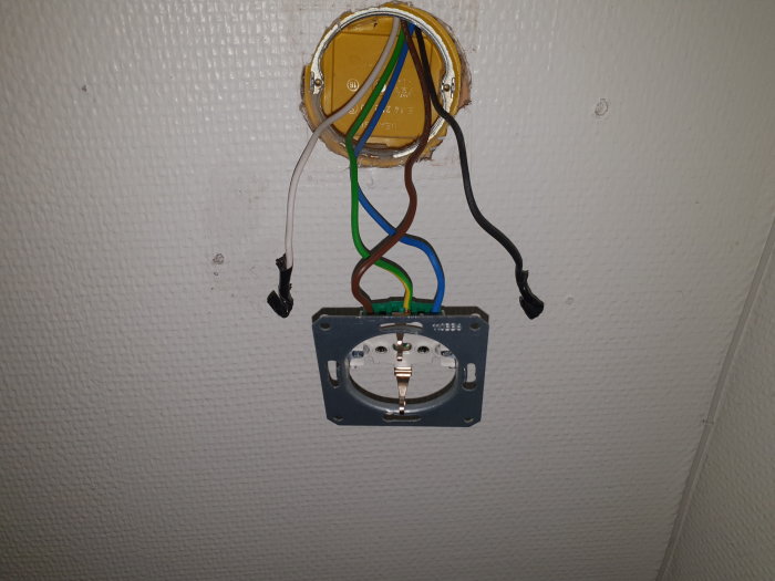 Öppen eldosa med utstickande kablar och borttaget eluttag på en vägg.