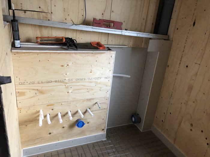 Pågående badrumsrenovering med plywoodväggar, rörinstallationer och byggverktyg.