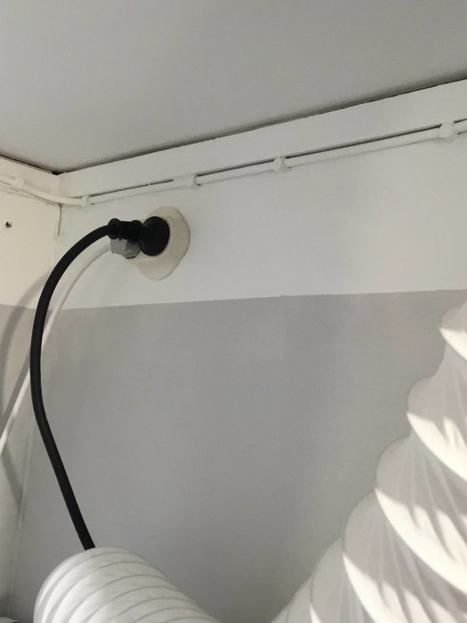 Vägguttag med ansluten kabel ovanför vit torktumlare i en tvättstuga.