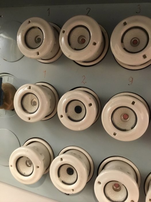 Närbild på en gammal elcentral med flera keramiska säkringar och numrerade säkringsplatser.