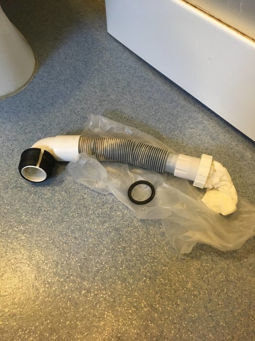 Gammalt flexibelt avloppsrör med skador bredvid duschkabinen, redo att bytas ut.