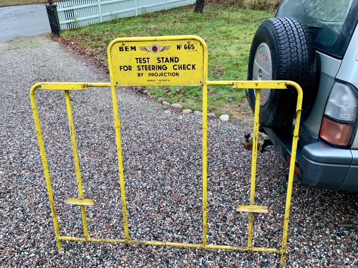 Gul ställning med skylten "TEST STAND FOR STEERING CHECK" framför en bil.