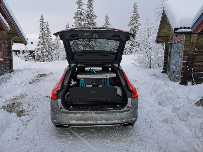 Baklucka öppen på bil i snöigt landskap med en byggsåg och verktygslådor lastade.