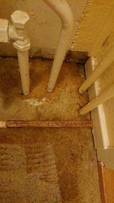 Mätning av avståndet vid tröskel med tumstock nära rörledningar på ett betonggolv.