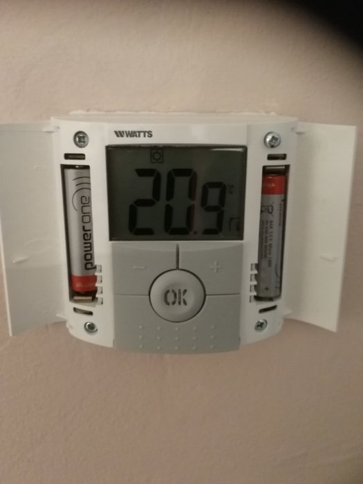 Digital värmetermostat visar 20.9 grader Celsius, termostatens ikoner indikerar värmepåslag. Batterier synliga.