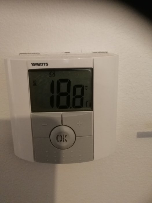 Digital termostat visar inomhustemperatur på 18,6 grader Celsius mot en vit vägg.