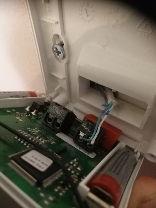 Inkoppling av termostat med turkos och vit sladd i golvvärmesystem.