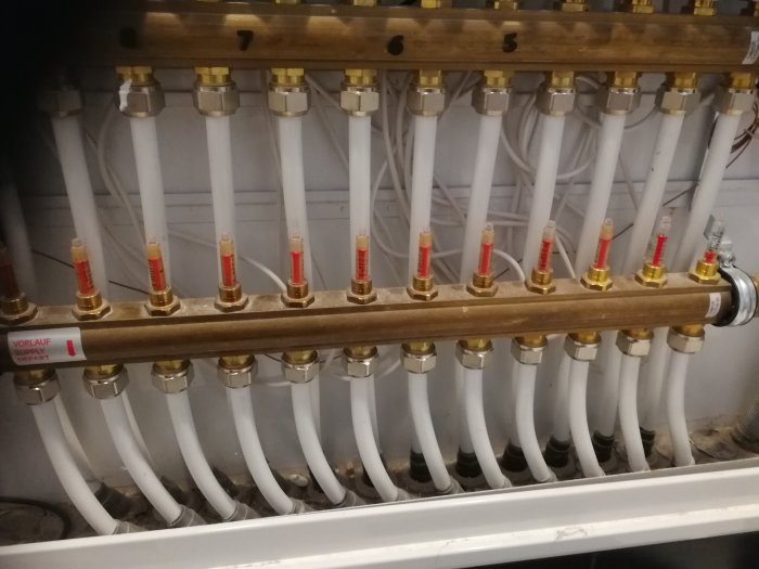 Mässingsfördelare med vita pexrör och röda mätinstrument för värmeinstallation, med fråga om pumpavstängning.