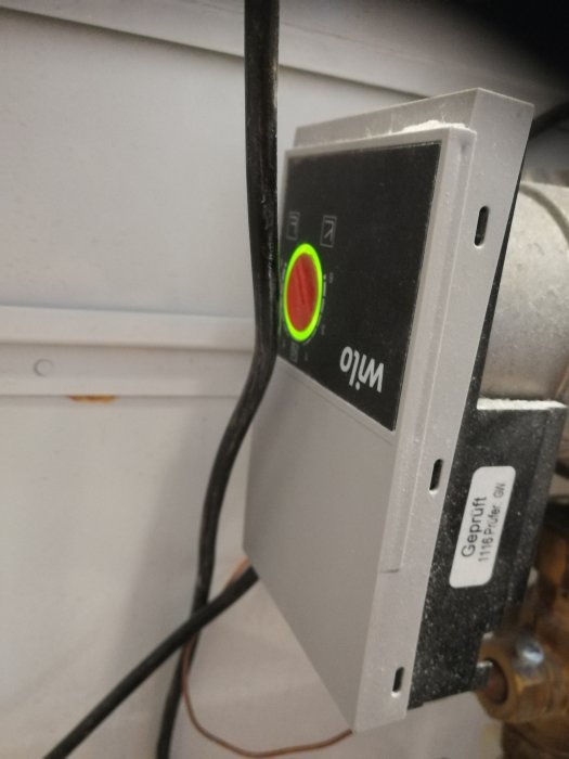 En tänd strömbrytare med en grön lysande ring runt knappen, monterad på en vägg med kablar som löper bakom.