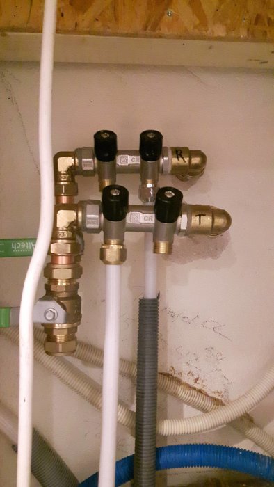Rörkopplingar och ventiler på en tappvattenfördelare monterade på en vägg.