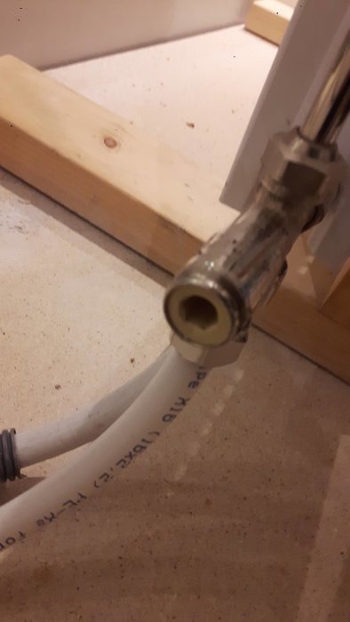 Närbild av en delvis utskruvad tappvattenfördelare ansluten till en vit plastslang.
