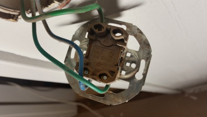 Gammal trappströmbrytare med grön och blå kabel i eluttag nära tak.