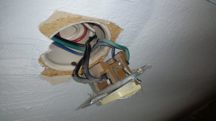 Gamla eluttaget öppnat i väggen med synliga kablar och elledningar.