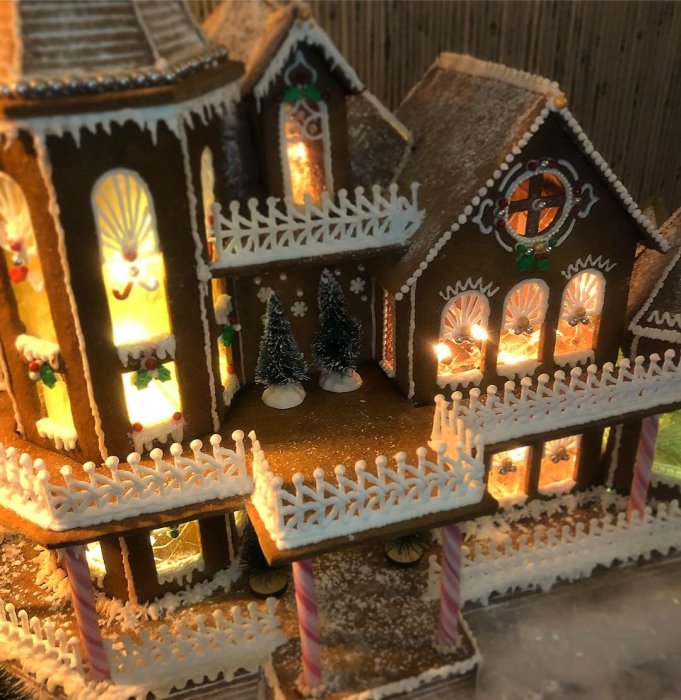 Detaljerat pepparkakshus med belysning, dekorationer och granar.