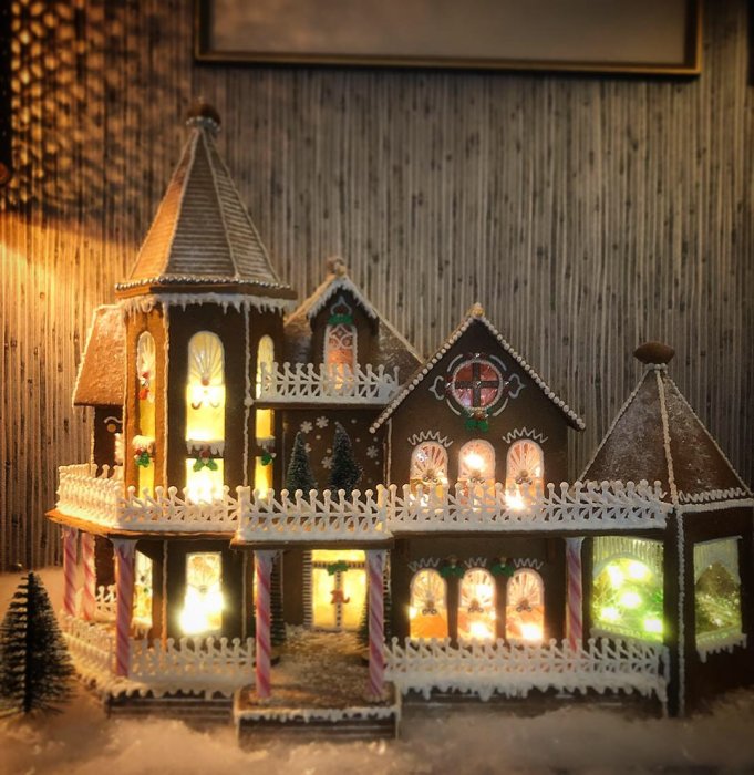 Modell av ett julpepparkakshus med upplysta fönster, detaljerade dekorationer och snöeffekt.