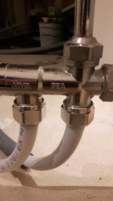 Metallrör och kopplingar för vatteninstallation, med fokus på en T-koppling och anslutna flexibla rör.