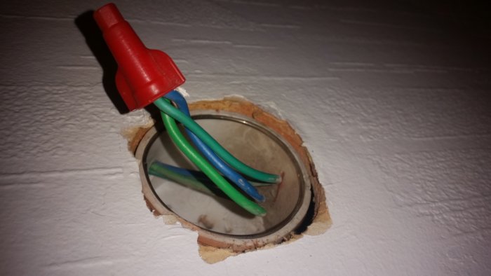 Elektrikerarbete med en väggdosa där elektriska kablar är ihopkopplade med en röd kabelsko.