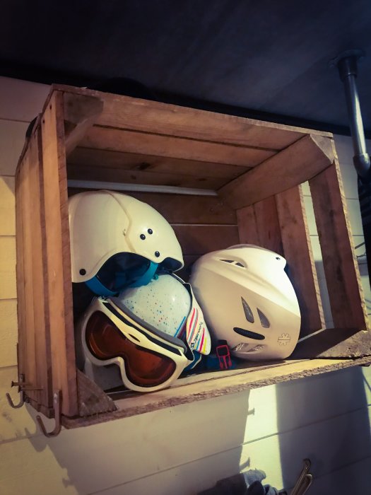 Trähylle innehållande skidhjälmar och goggles med laminattak i bakgrunden.