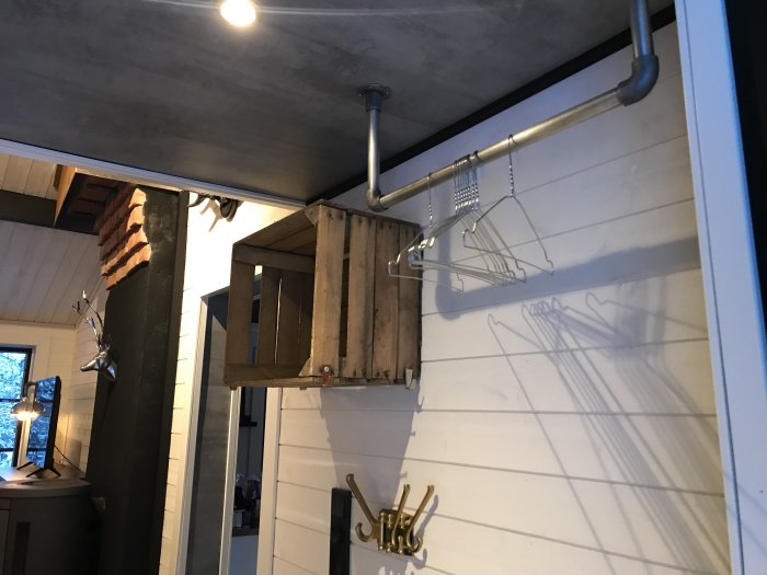 Hall med vit panelvägg, svart pelare, laminattak som liknar betong och industriell klädstång med kläder.