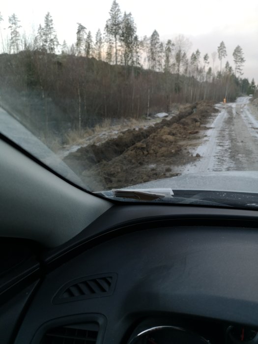 Grävd fåra för optikfiberkabel sett från en bil längs en skogsväg.