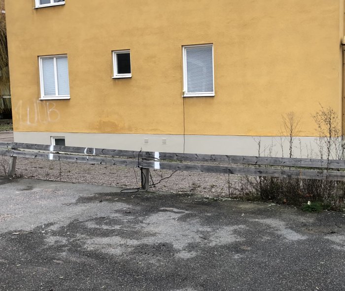 Motorvärmaruttag monterat genom fönsterkarm på gult hus, kabel hänger längs vägg och staket.