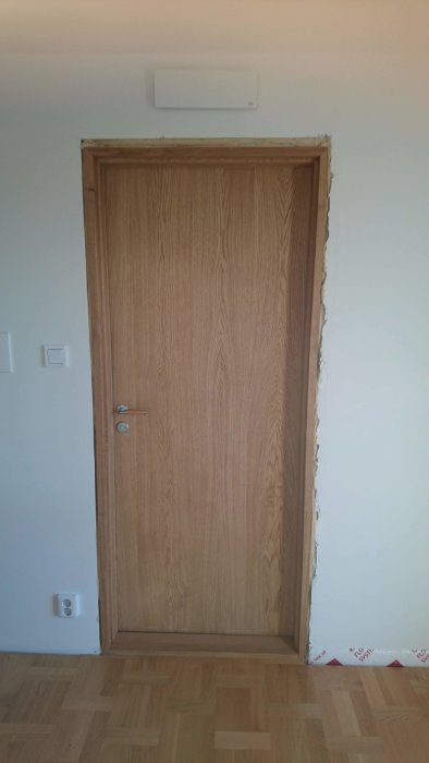 Nyinstallerad innerdörr i ek utan foder, synlig isolering och glipa vid tröskeln.