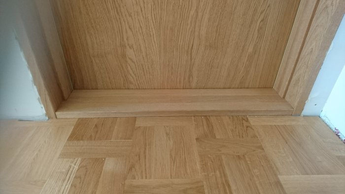 Nyinstallerad massiv ekdörr med tätning och 2 mm glipa mot tröskeln på ett trägolv.