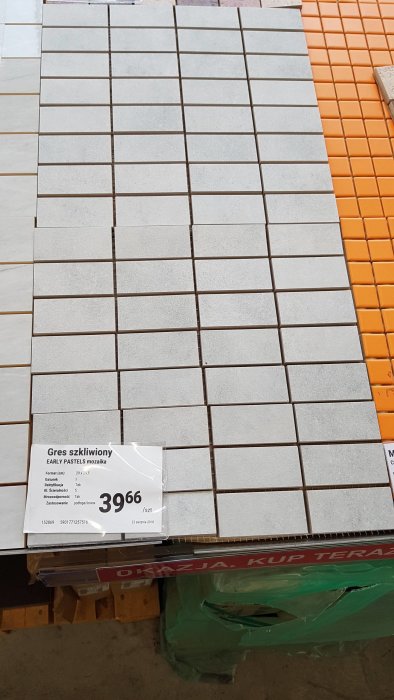 Grå och orange mosaikplattor på en butikshylla med prisetikett, avsedda för badrumsgolv och vägg.