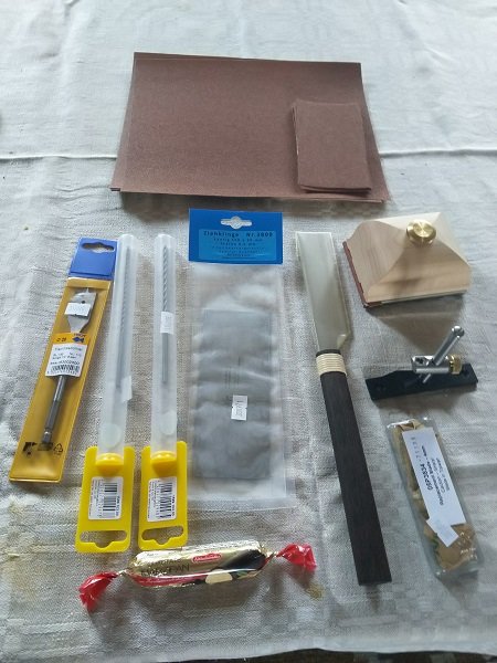 Byggmaterial inköp inklusive sandpapper, sågblad, borrstål och tysk marsipankonfekt på ett tygunderlag.