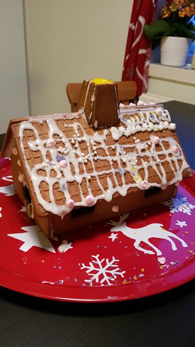 Pepparkakshus med dekorationer och en synlig spricka i väggen på ett rött serveringsfat.