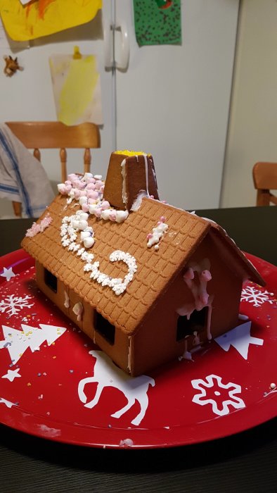 Pepparkakshus med sprickor och kreativ dekoration av godis och glasyr gjord av barn.