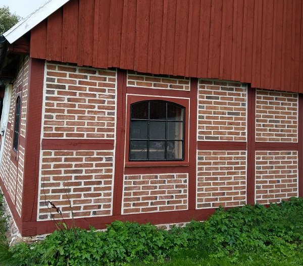 Stallfönster med innerbågar på en tegelvägg och järnfönster nyfogat i träkarm.