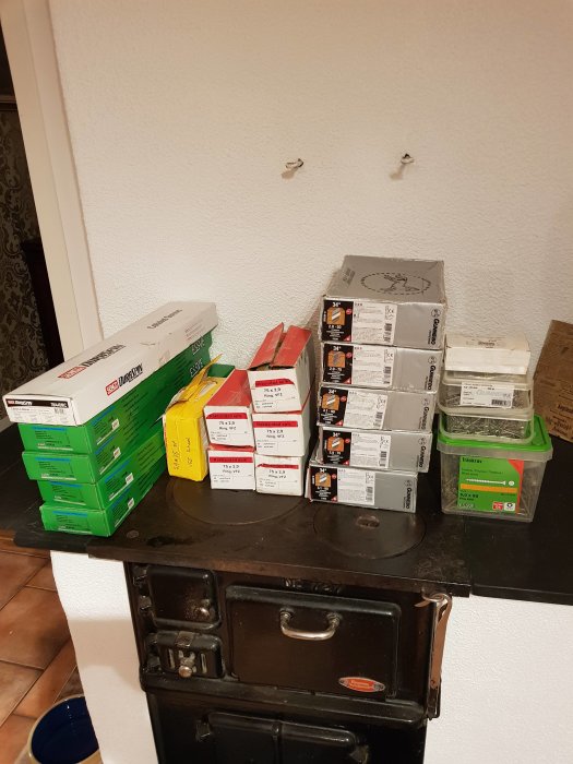 Byggmaterial som skruvlådor och spikförpackningar på en gammal svart spis.