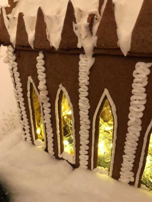 Pepparkakshus inspirerat av Hogwarts med snö och kristyrdekorationer samt lysande fönster.