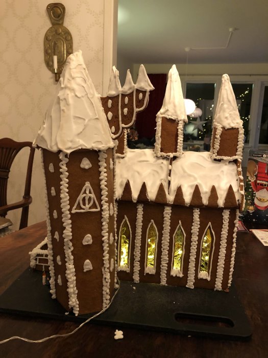 Hemmagjord pepparkakskreation av Hogwarts slott i snö med kristyr och belysta fönster.