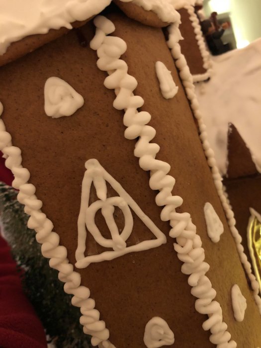 Pepparkakshusvägg dekorerad med kristyr som föreställer Hogwarts i snö med dödsrelikerna-symbolen.