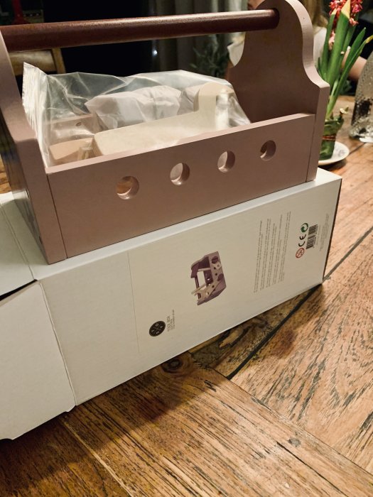 Förpackad barnsak i en gåva för dop, med synligt märke och trädetaljer på en trägolv.